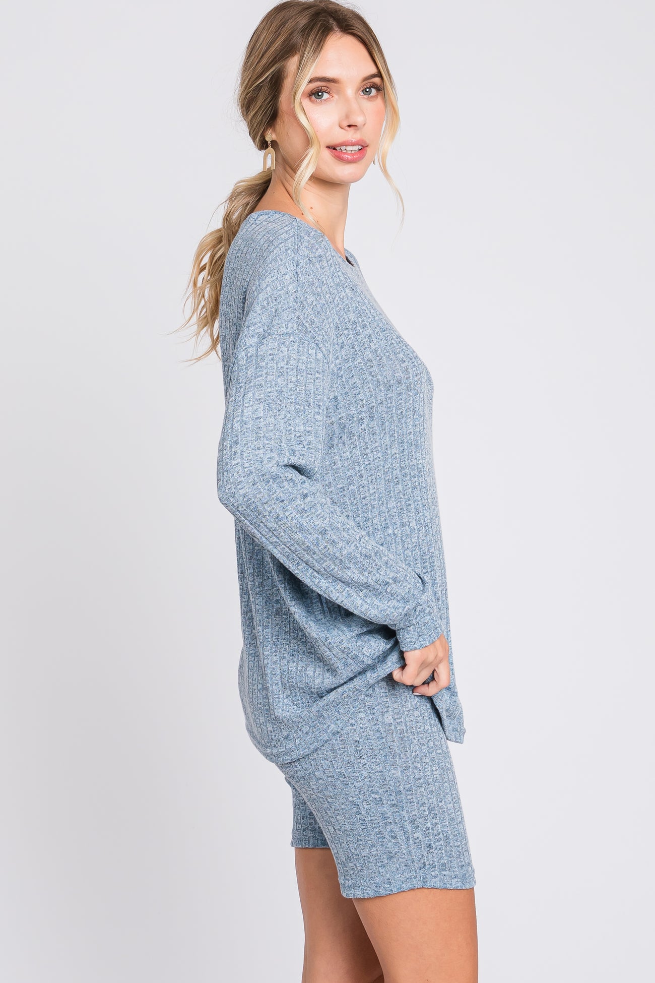 woman wearing a light blue ribbed sweater and matching shorts, posing sideways against a plain background