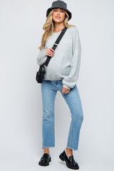 woman wearing a gray oversized sweater and light blue jeans with a baby bump, accessorized with a black bucket hat and bag