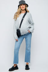 woman wearing a gray oversized maternity sweater and light blue cropped jeans with a black bucket hat and crossbody bag