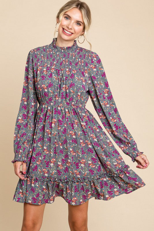 woman wearing a smocked floral gray mini dress with long sleeves and ruffle hem