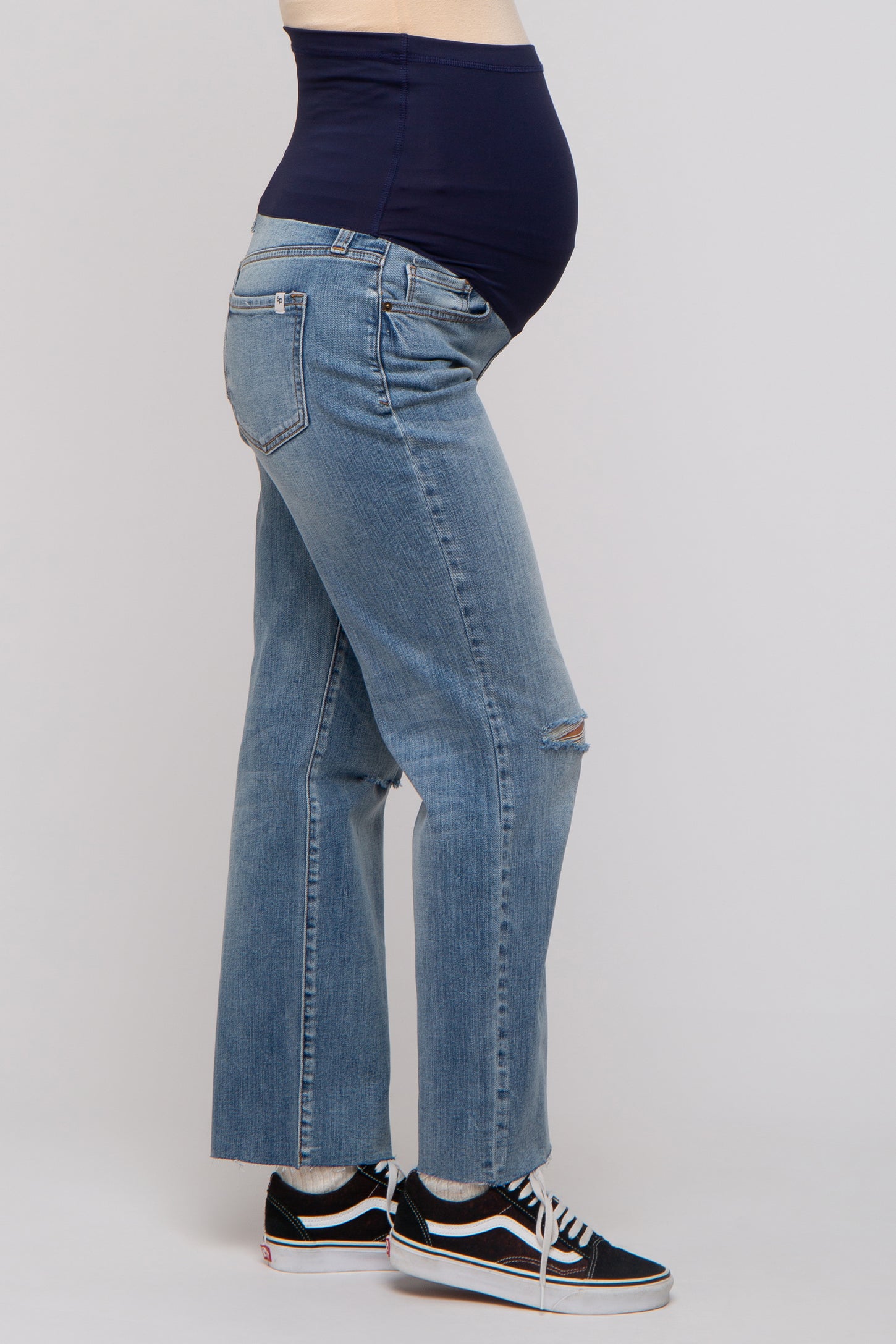woman wearing a pair of light blue maternity jeans with a navy blue over-the-bump panel and a visible baby bump