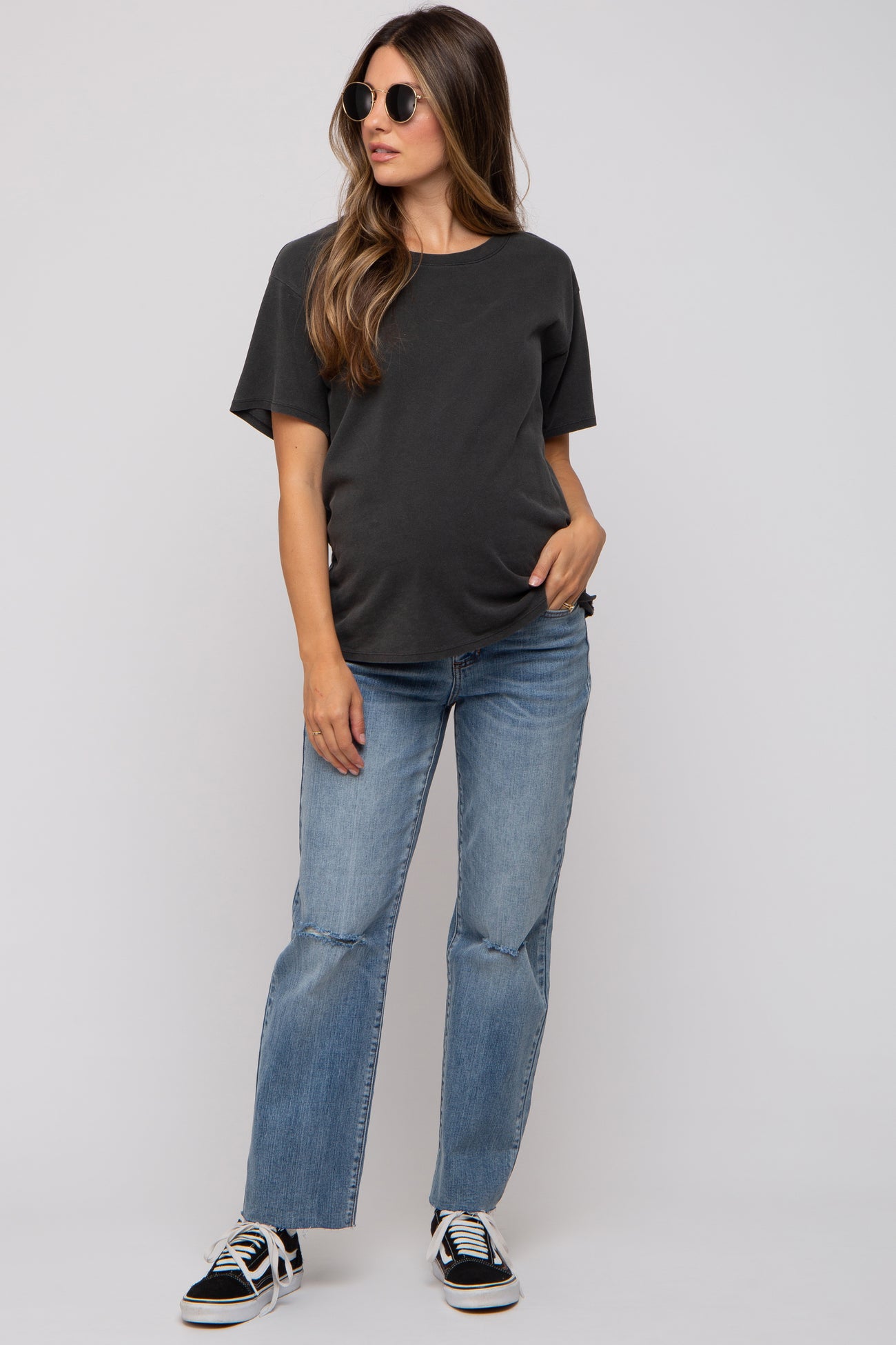 woman wearing a black short sleeve maternity top and light blue jeans, showing her baby bump and styled with sunglasses