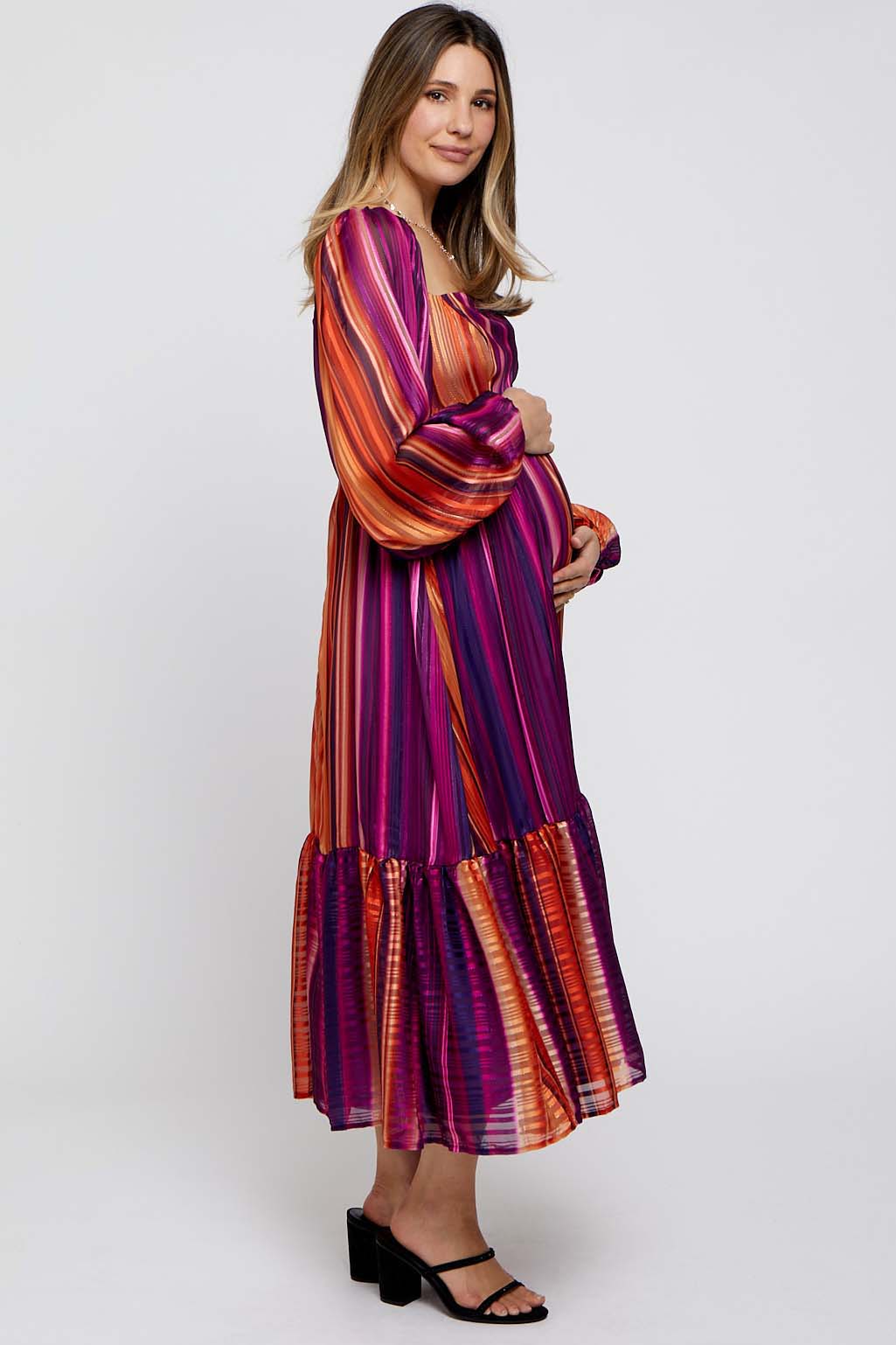 woman wearing a long sleeve purple and orange striped maternity dress with ruffled hem and gently holding her baby bump