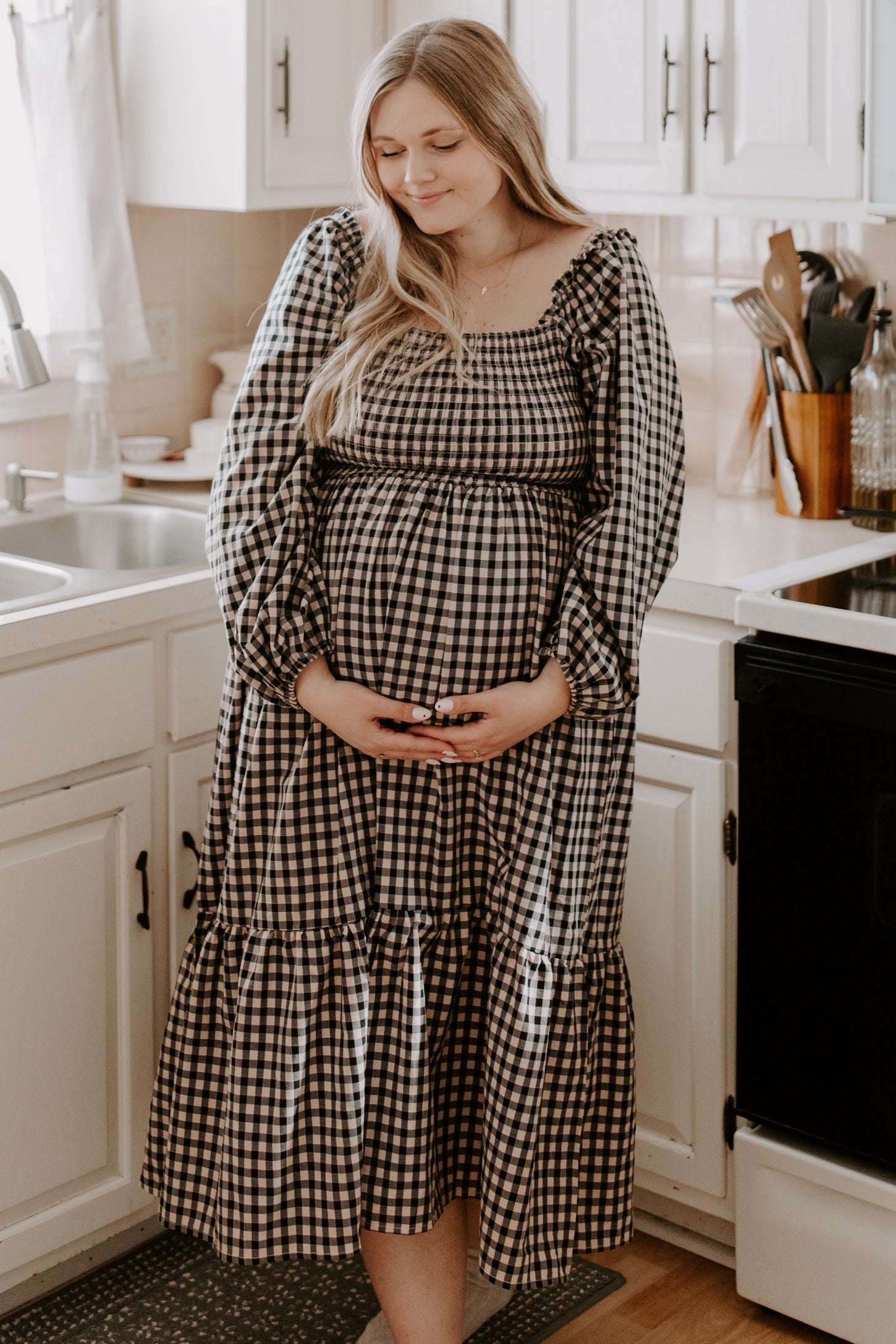 woman wearing a black and white gingham maternity dress with a tiered skirt and holding her baby bump