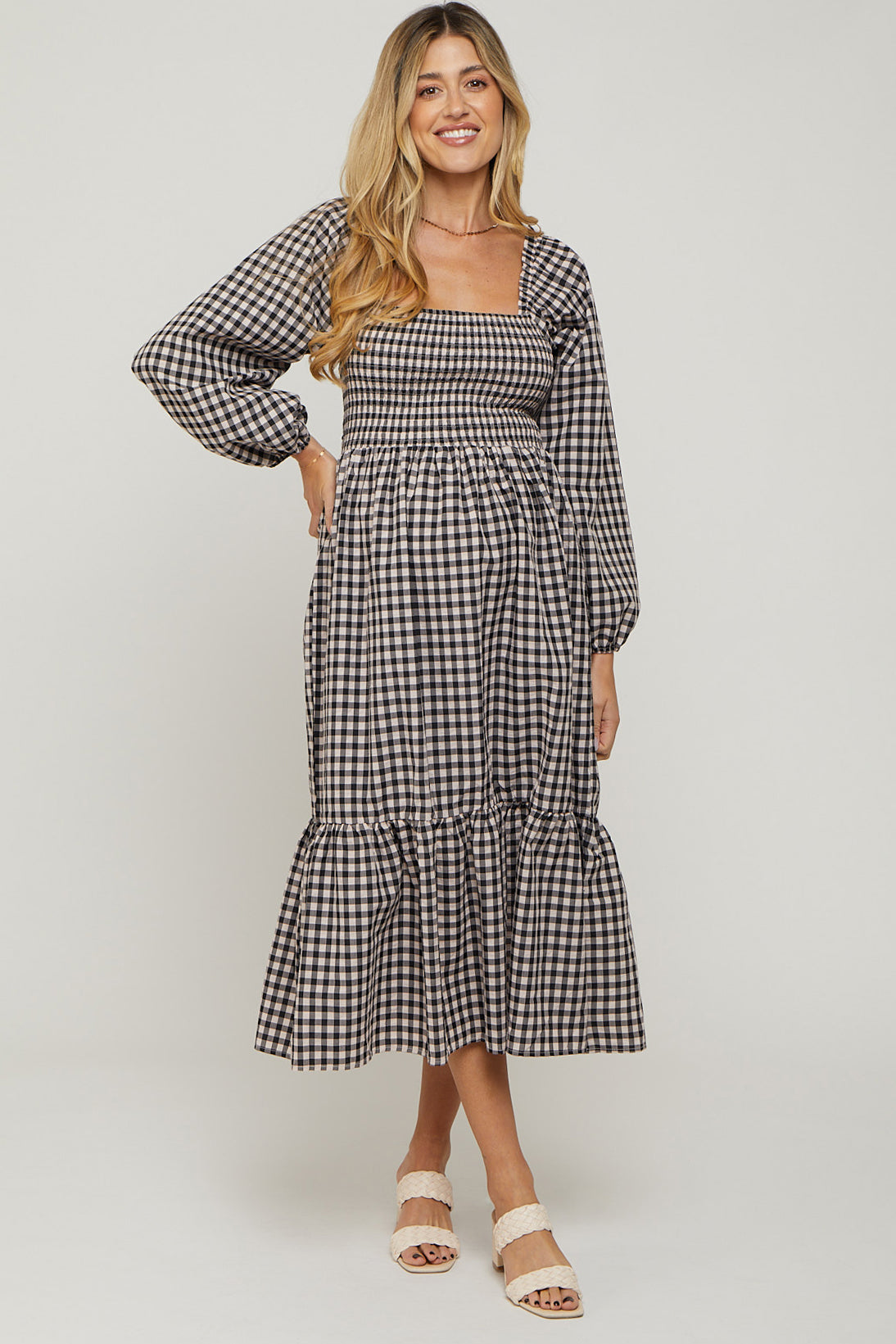 woman wearing a black and white gingham maternity dress with long sleeves and ruffle hem, showcasing her baby bump