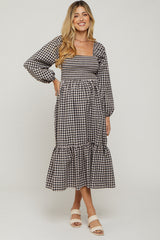 woman wearing a black and white gingham maternity dress with long sleeves and ruffle hem, showcasing her baby bump