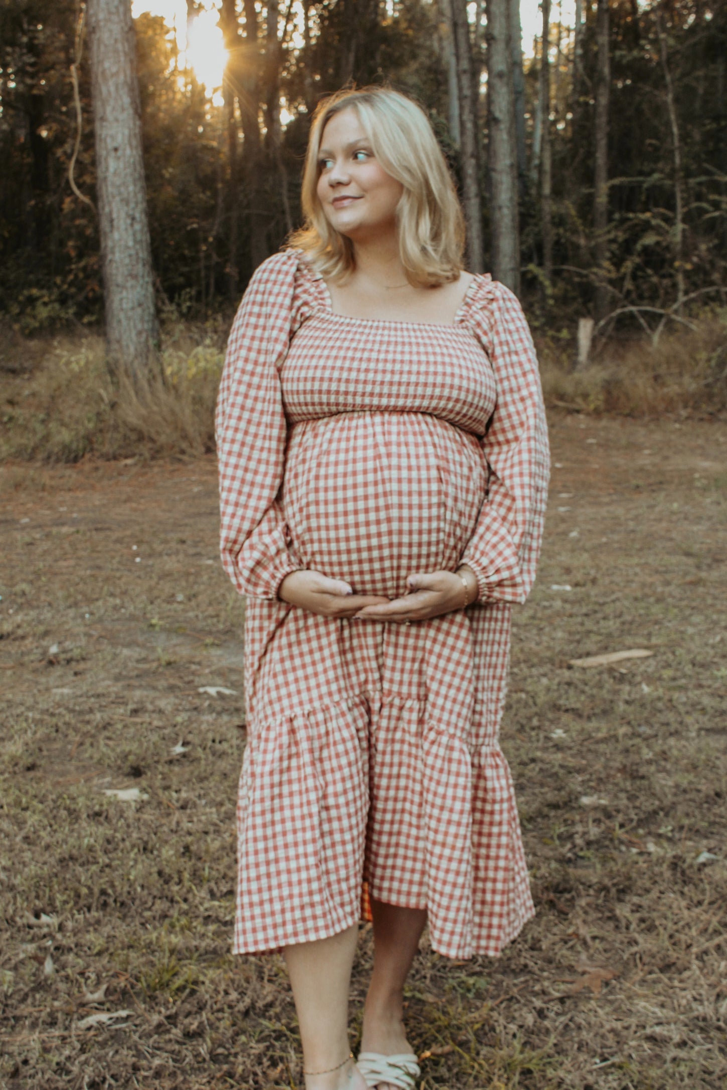 woman wearing a pink and white gingham maternity dress with puff sleeves and a ruffled hem, holding her baby bump
