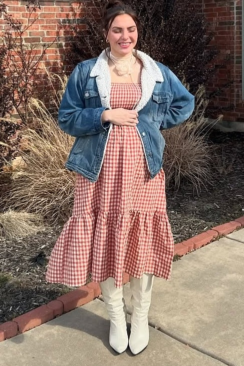 woman wearing a red and white gingham maternity dress with a tiered skirt, styled with a denim jacket and knee-high white boots
