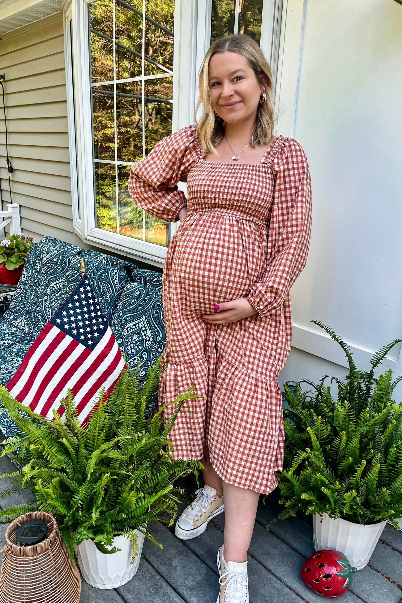woman wearing a brown and white gingham maternity dress with long sleeves and holding her baby bump