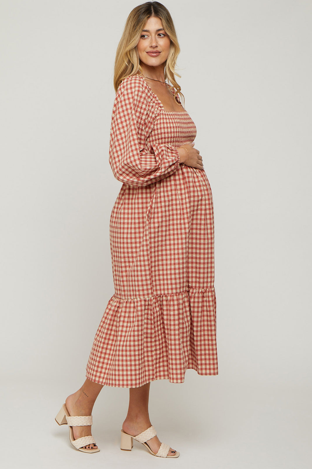 woman wearing a red and white checked maternity dress with a square neckline and ruffle hem, gently cradling her baby bump