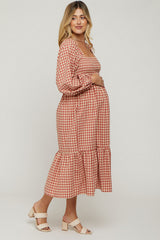 woman wearing a red and white checked maternity dress with a square neckline and ruffle hem, gently cradling her baby bump
