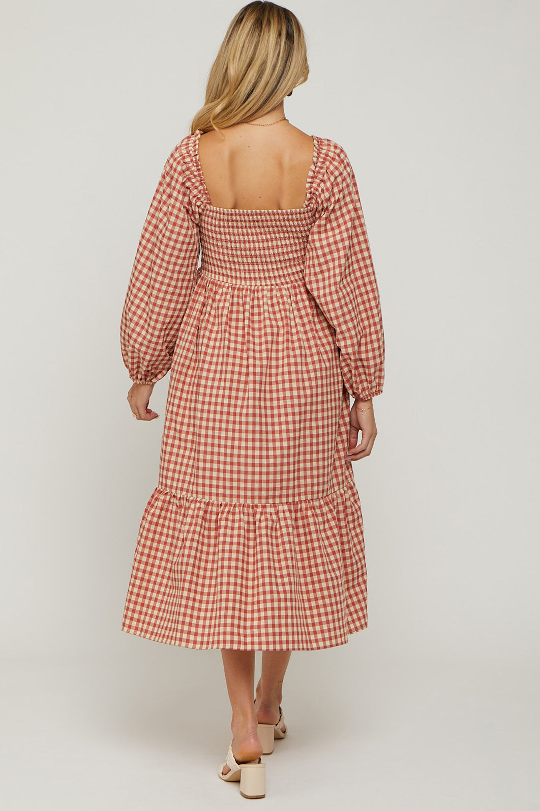 woman wearing a pink and white gingham maternity dress with puff sleeves and a tiered skirt, showing her baby bump