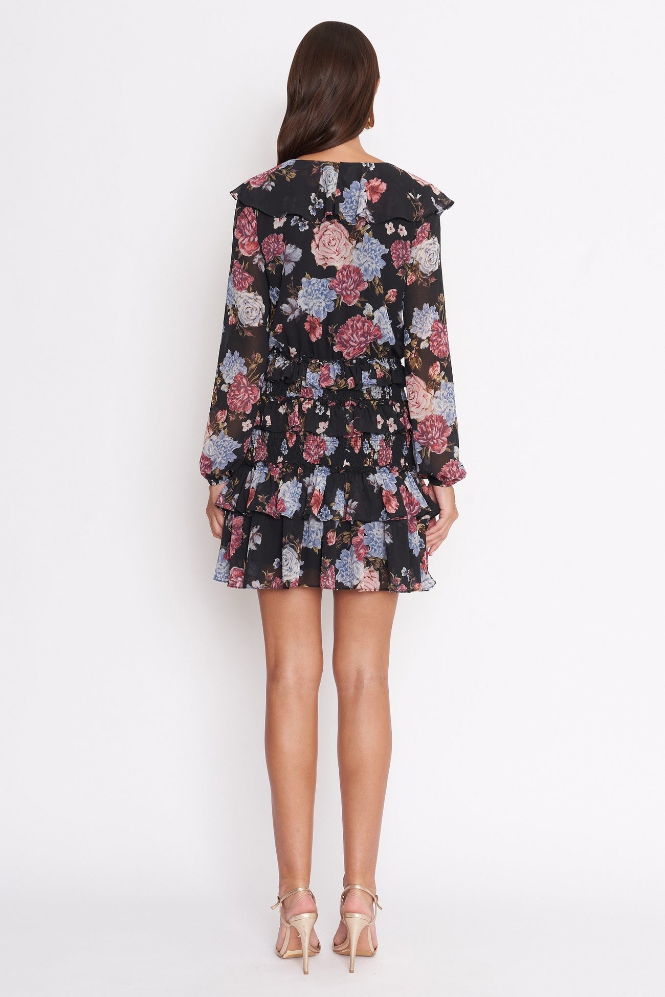 woman wearing a black floral mini dress with long sleeves and ruffled hem, shown from the back
