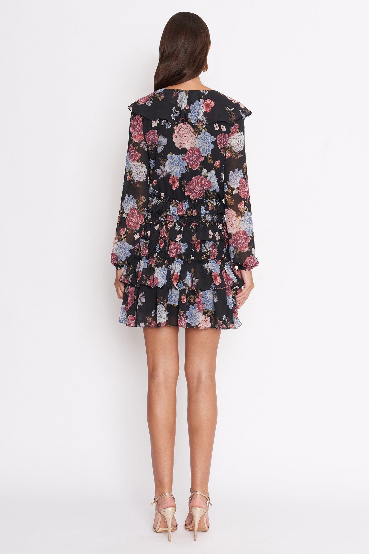 woman wearing a black floral mini dress with long sleeves and ruffled hem, shown from the back