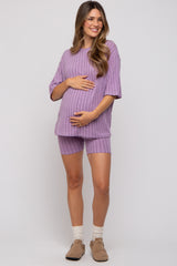 woman wearing a lavender ribbed maternity set consisting of a short-sleeve top and matching shorts, cradling her baby bump