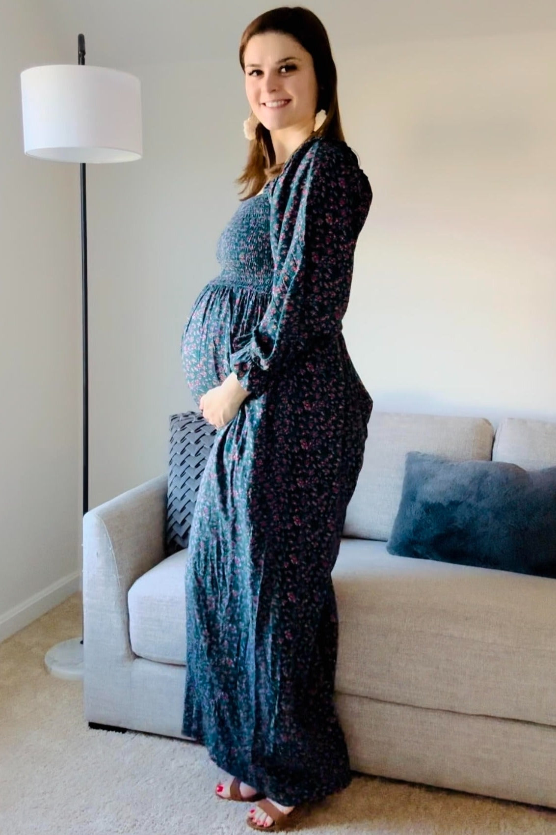 woman wearing a dark floral maternity maxi dress and holding her baby bump