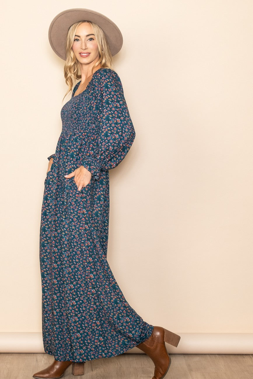 woman wearing a navy floral maxi dress with balloon sleeves and pockets, styled with a wide-brim hat and brown ankle boots