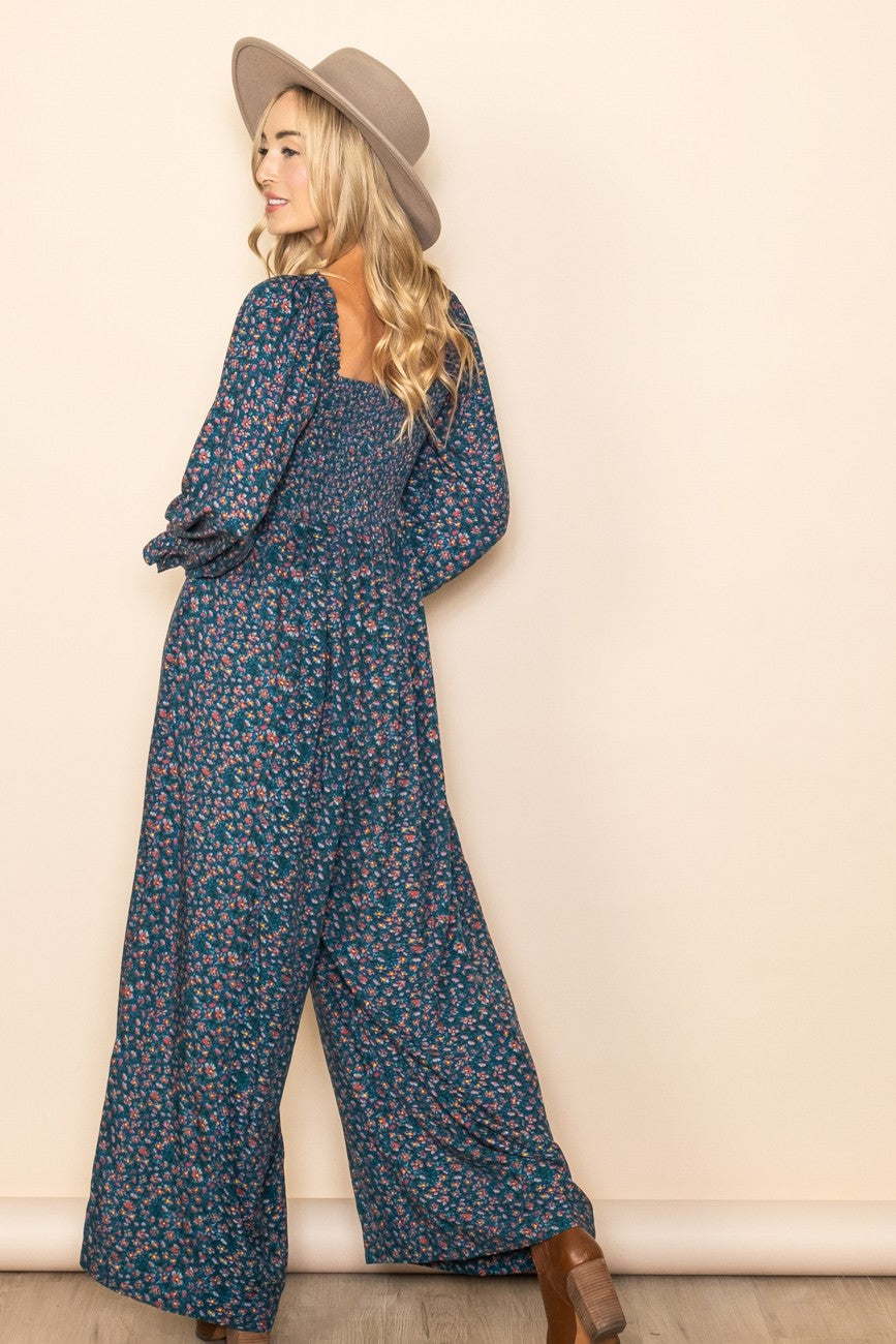 woman wearing a navy floral print jumpsuit with long sleeves and a smocked bodice, styled with a wide-brimmed hat