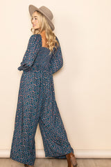 woman wearing a navy floral print jumpsuit with long sleeves and a smocked bodice, styled with a wide-brimmed hat