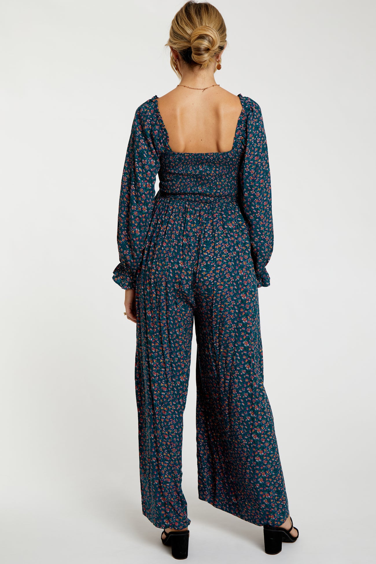 woman wearing a dark floral maternity jumpsuit with a smocked bodice and long sleeves, shown from the back