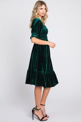 woman wearing a dark green velvet midi dress with puff sleeves and a ruffled hem