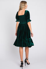 woman wearing a dark green velvet dress with puff sleeves and a tiered hem, viewed from the back