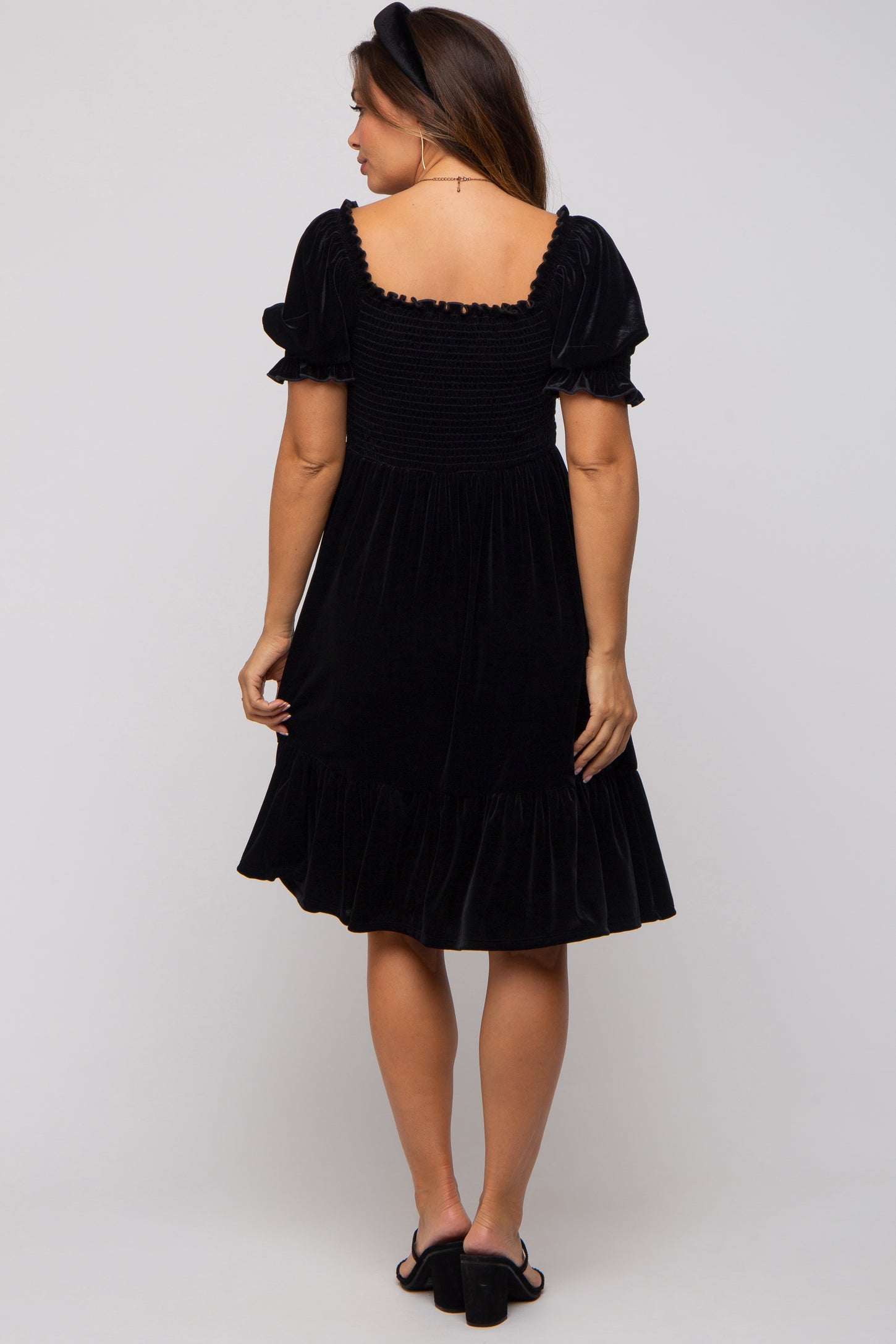 woman wearing a black velvet maternity dress with short puff sleeves and a ruffled hem, showing her baby bump from the back
