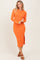 woman wearing a long sleeve orange ribbed midi dress with a side slit and styled with brown sandals