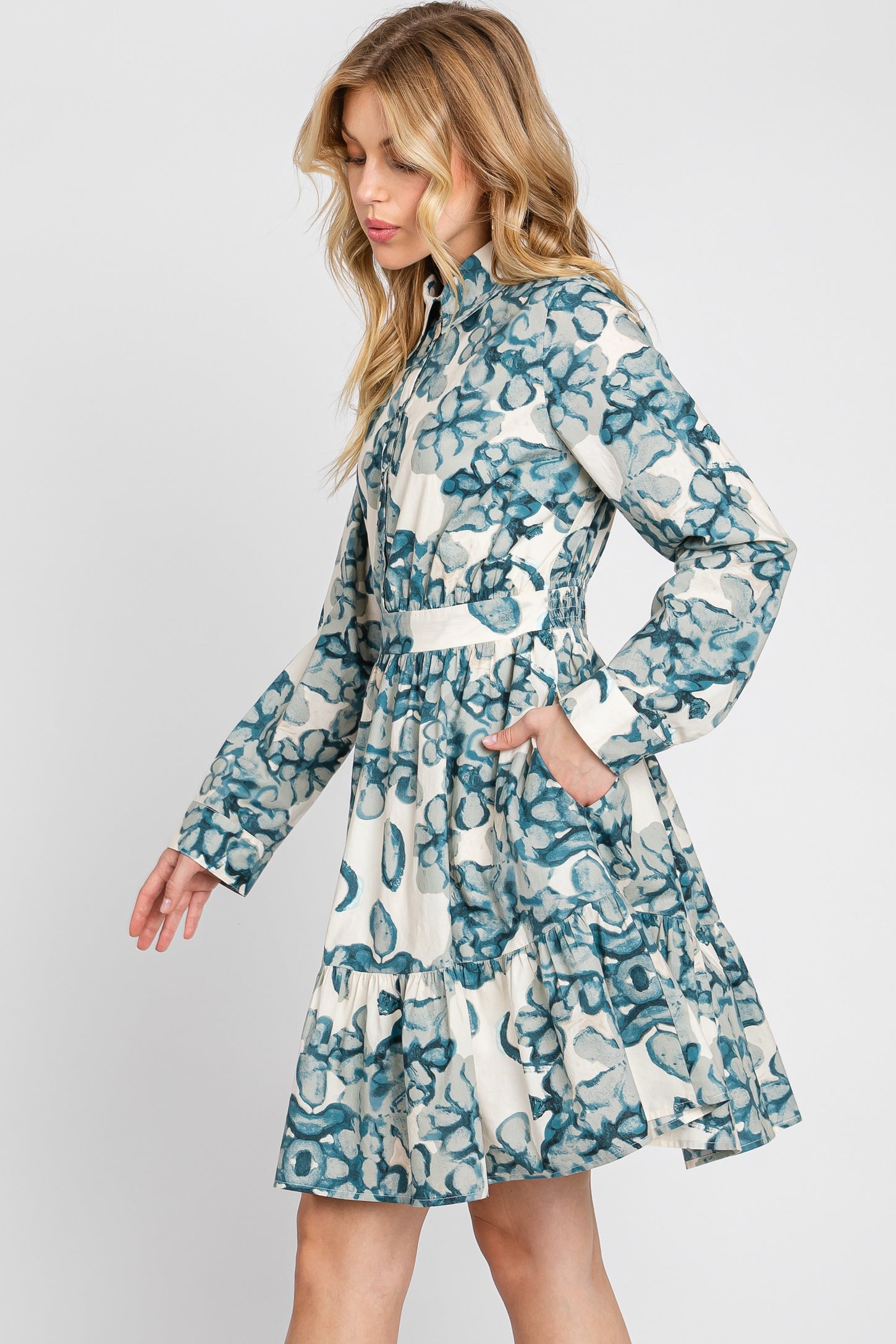 woman wearing a floral print long sleeve dress with a tiered skirt and pockets, in shades of blue and white