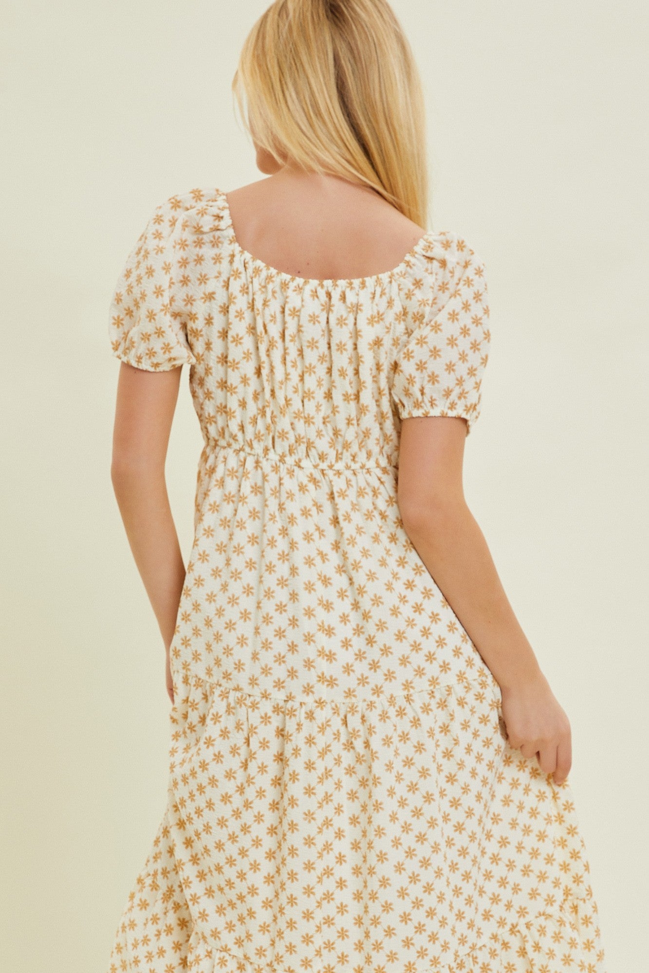 woman wearing a white tiered maxi dress with yellow floral print and puff sleeves, seen from the back