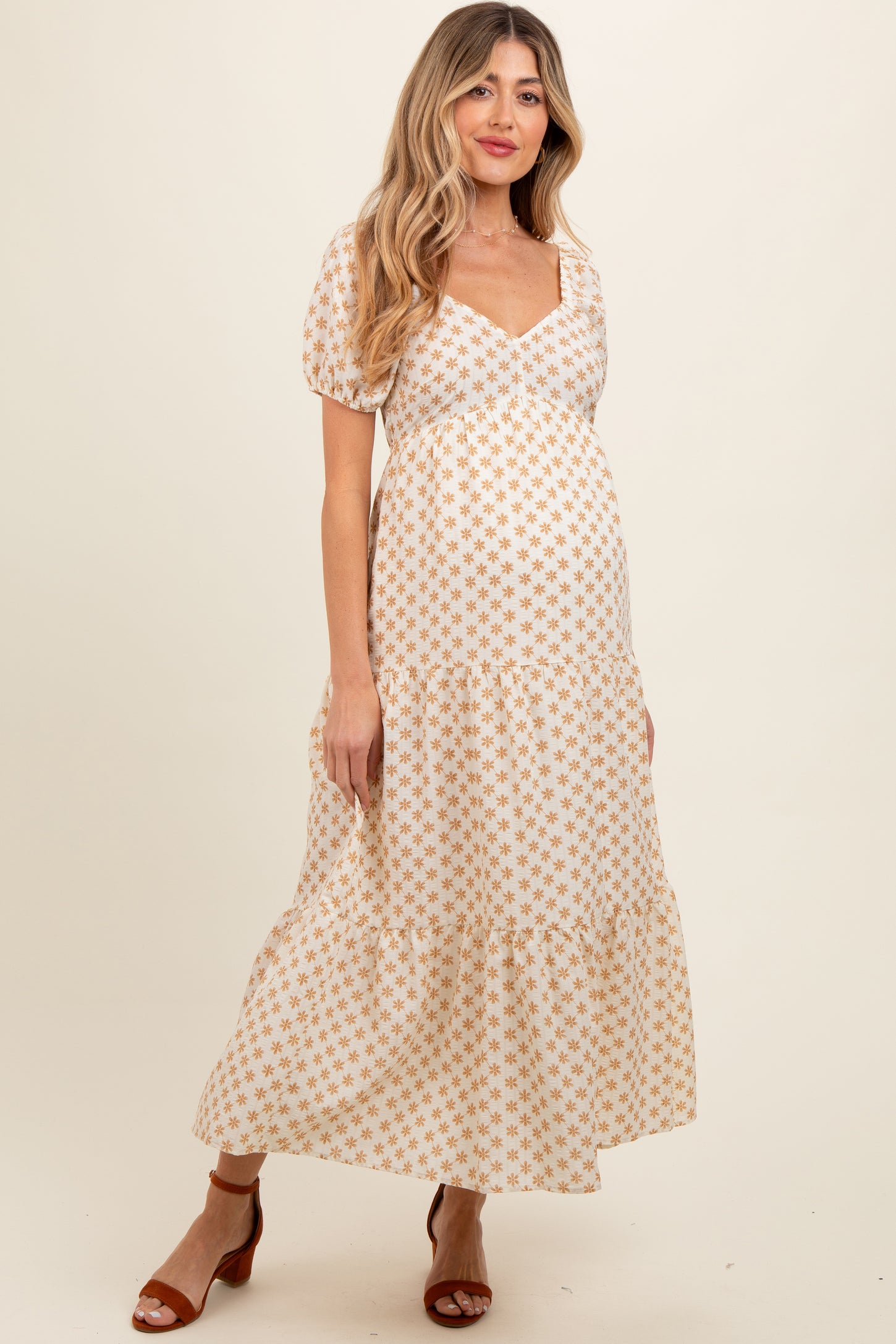 woman wearing a white floral print maternity maxi dress with puff sleeves and a tiered skirt, showing her baby bump