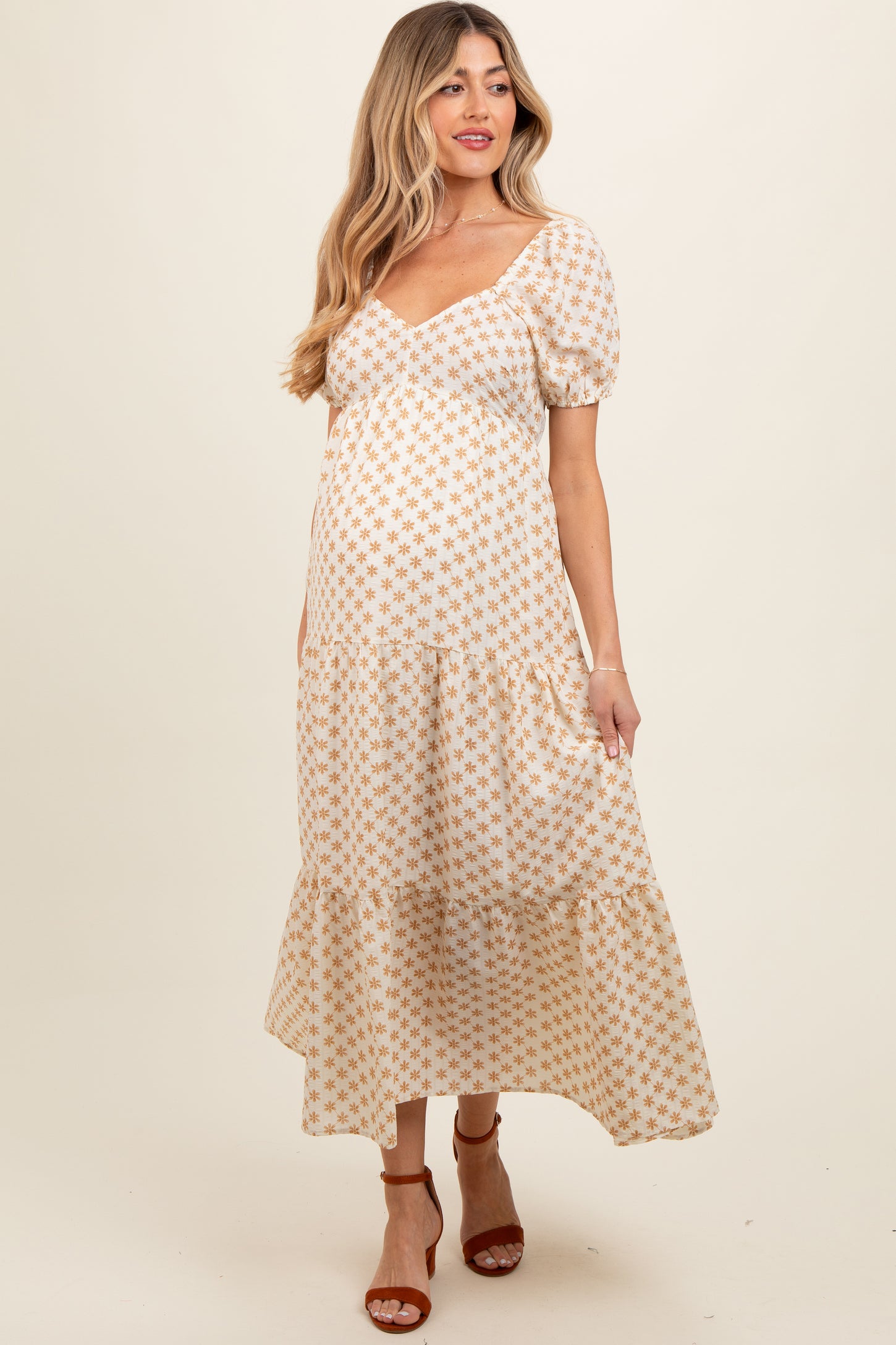 woman wearing a cream maternity maxi dress with a floral pattern and puff sleeves, showing her baby bump