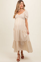 woman wearing a cream maternity maxi dress with a floral pattern and puff sleeves, showing her baby bump