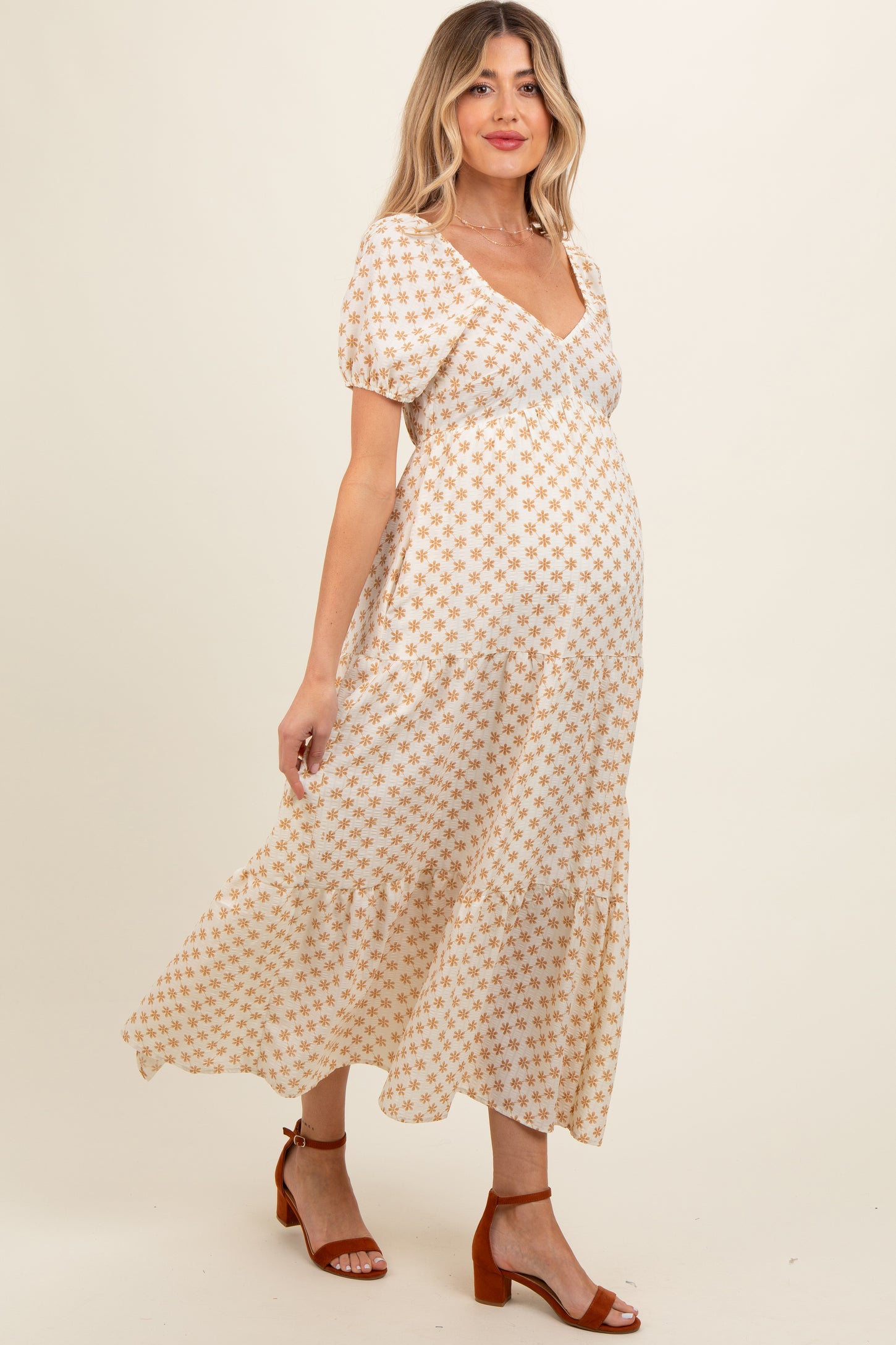 woman wearing a cream floral print maternity dress with puff sleeves and a tiered skirt, showing her baby bump