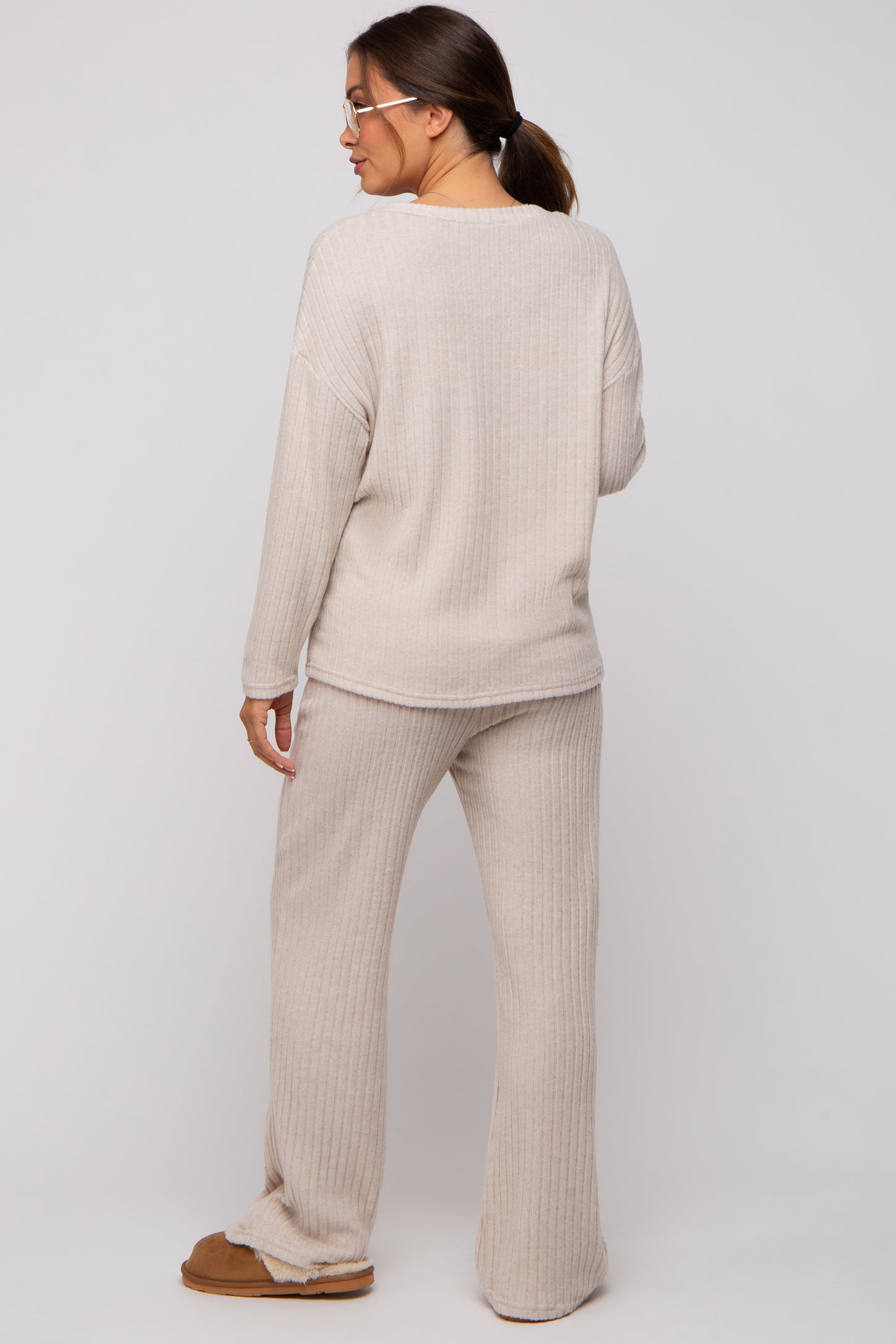 woman wearing a beige ribbed maternity loungewear set with long sleeves and wide-leg pants, showing a relaxed fit from behind