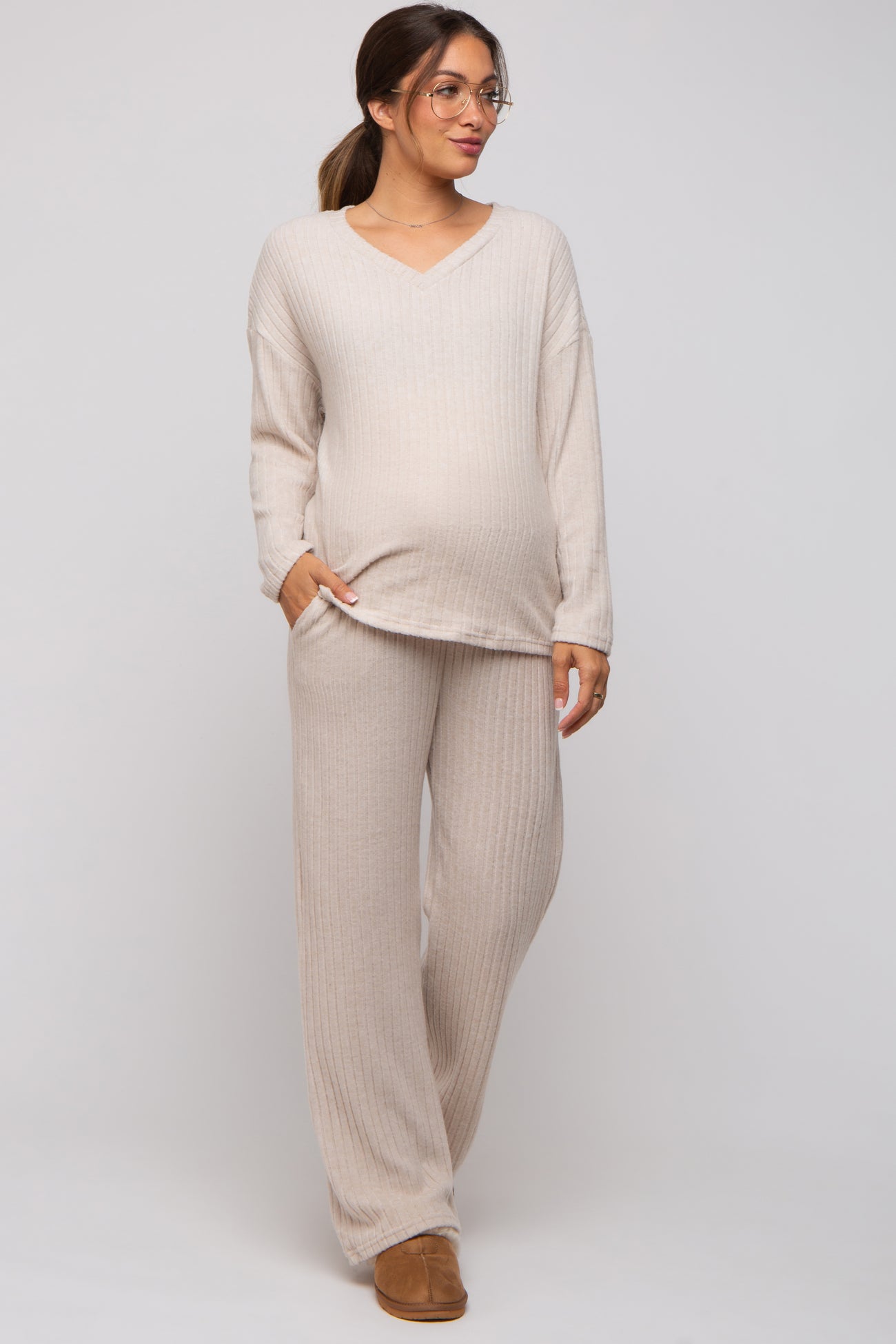 woman wearing a beige ribbed maternity top and matching pants, showcasing her baby bump, styled with glasses and a relaxed fit