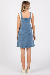 woman wearing a light wash denim overall dress with adjustable straps and two back pockets