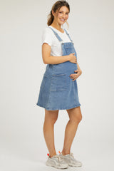 woman wearing a denim maternity overall dress, showcasing a visible baby bump, paired with a white t-shirt and sneakers