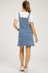 woman wearing a denim maternity dungaree dress with pockets, styled over a white t-shirt