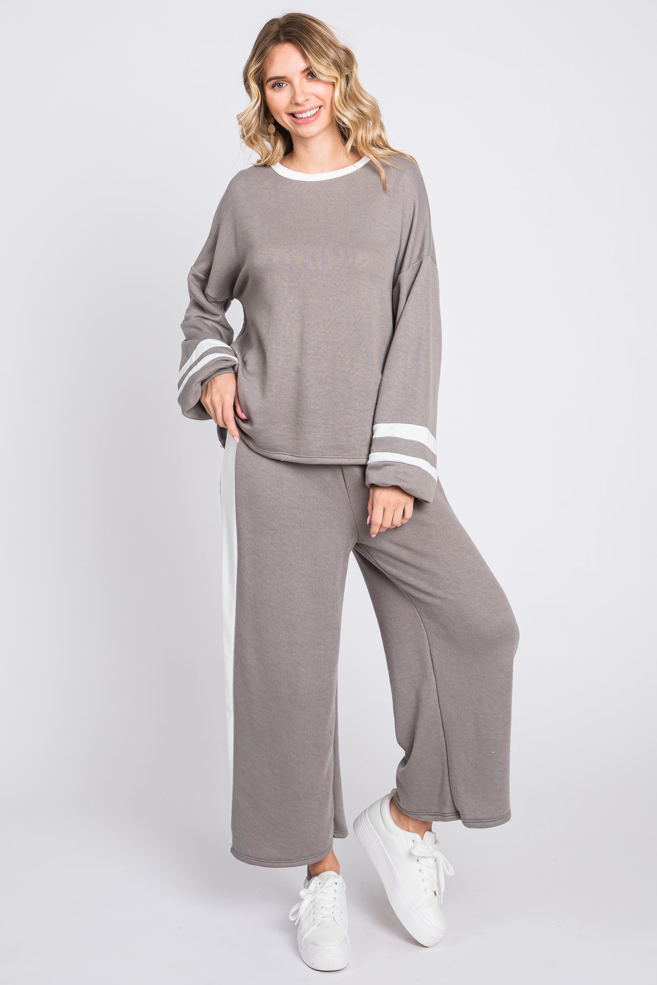 woman wearing a gray relaxed fit sweater and matching wide leg pants with white stripes, styled with white sneakers