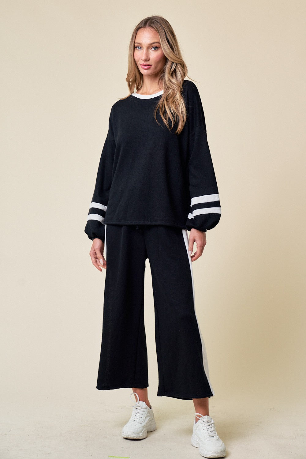woman wearing a black lounge set with white stripes on the sleeves and pants, paired with white sneakers