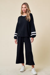woman wearing a black lounge set with white stripes on the sleeves and pants, paired with white sneakers