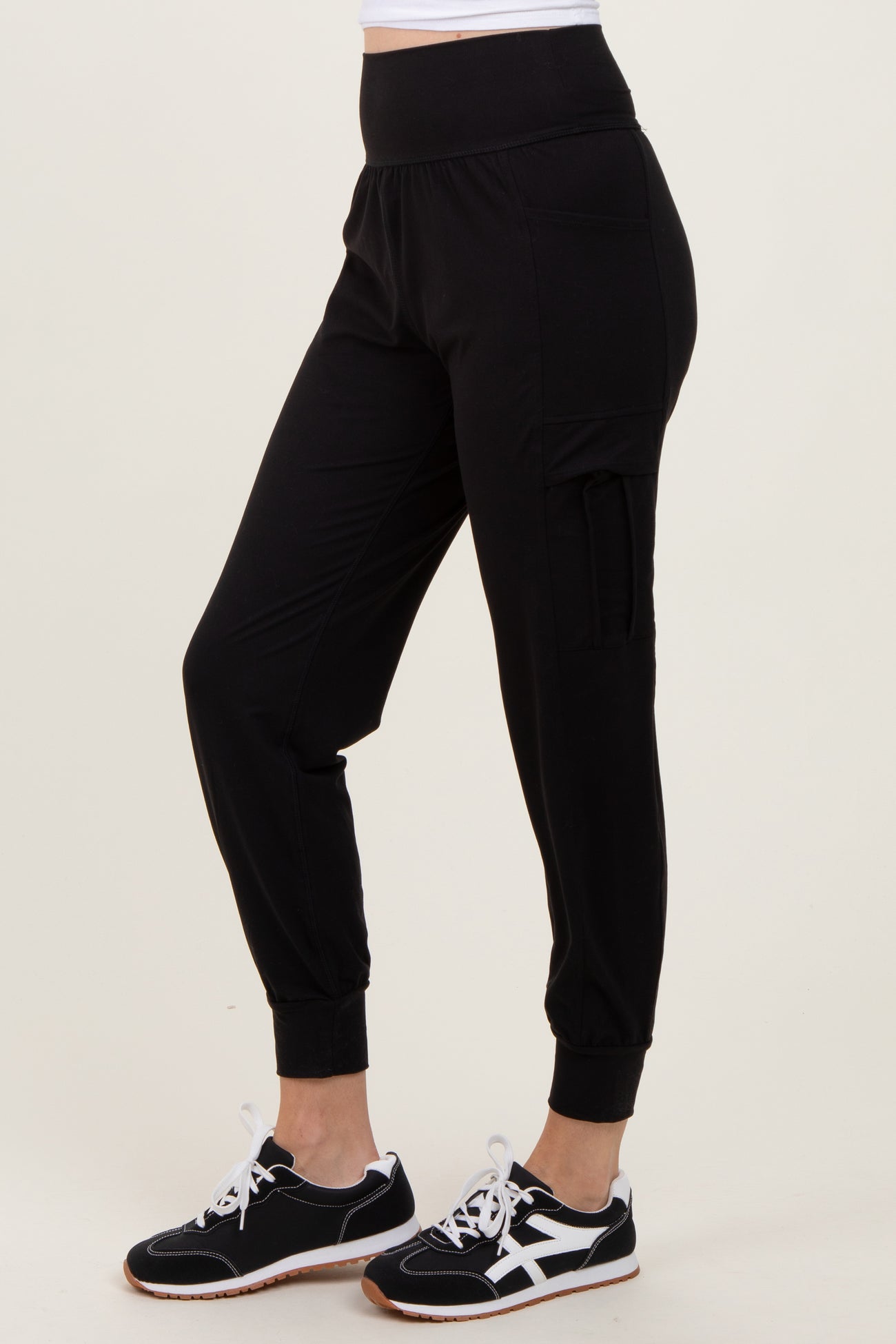 woman wearing black jogger pants with a high waistband and side pocket, paired with black and white sneakers