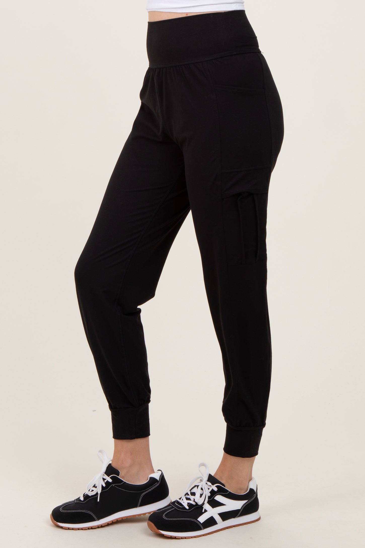 woman wearing black jogger pants with a high waistband and side pocket, paired with black and white sneakers