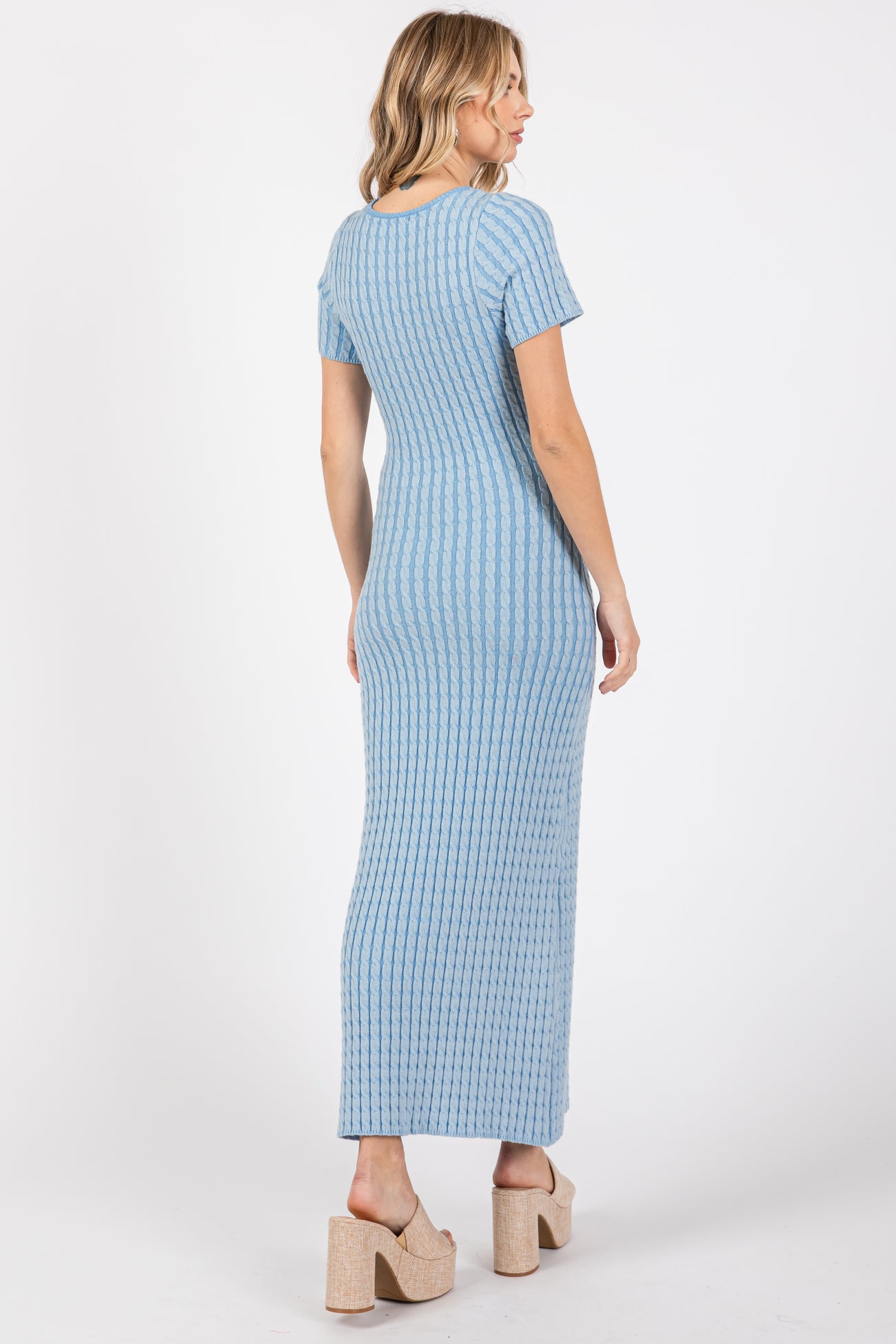 woman wearing a light blue ribbed maxi dress with short sleeves and a fitted silhouette, standing with her back to the camera
