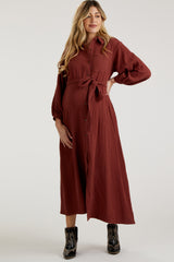 woman wearing a rust long sleeve button-up maternity dress with a tie waist and a visible baby bump