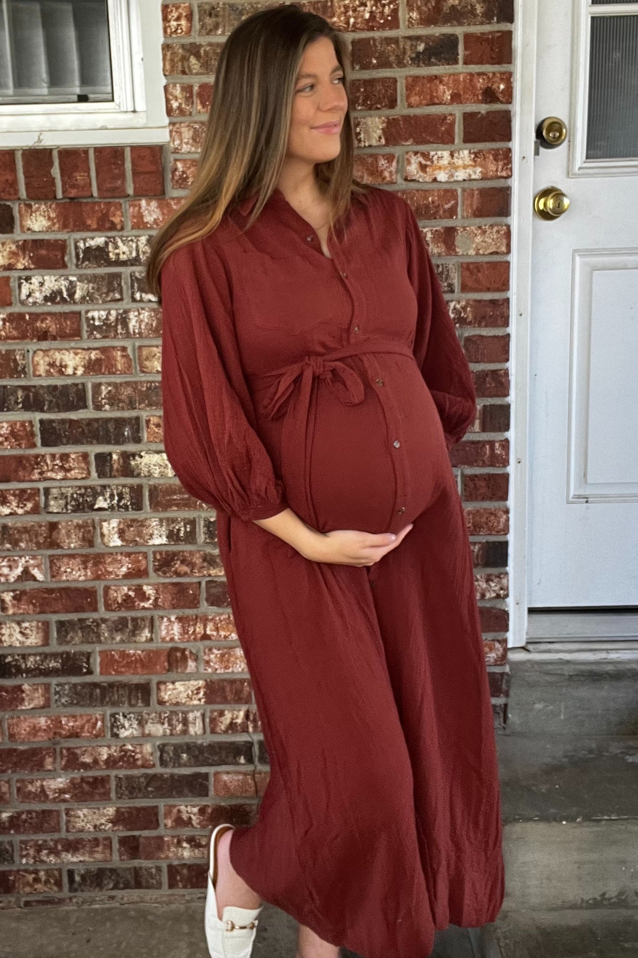 woman wearing a rust-colored long sleeve maternity dress with a tie waist and a visible baby bump