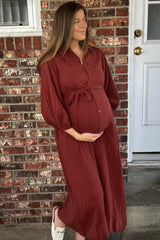 woman wearing a rust-colored long sleeve maternity dress with a tie waist and a visible baby bump