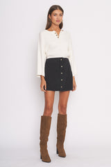woman wearing a white long sleeve henley top and a black button-front mini skirt with brown knee-high boots