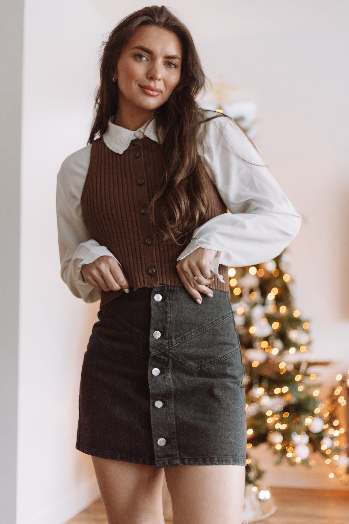 woman wearing a brown ribbed knit vest over a white blouse and a black button-up denim mini skirt
